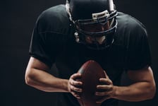 American football player with black helmet and armour running in motion holding ball getting ready to score a goal close up shot over dark background