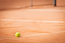 Yellow tennis ball on orange sand and white lines