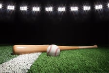 Baseball and bat at night under stadium lights on grass field