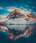 Antarctic landscape with snow covered mountains reflected in ocean water Sunset warm light on the mountain peak blue cloudy sky in the background Beautiful nature landscape Travel background